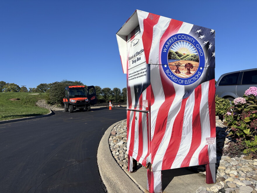 A ballot drop box designed to look like an American flag sits in a black asphalt parking lot.