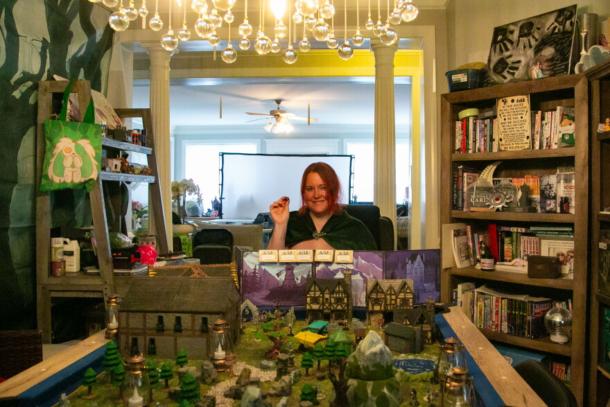 A woman with a board of houses, trees, and other structures for playing a game.