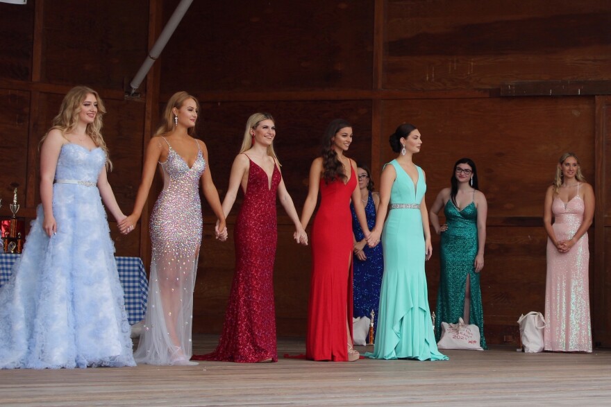 Women in long eveningwear hold hands in a line.