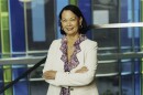 Ebert is standing with her arms crossed, smiling and wearing a purple shirt and a white jacket. 