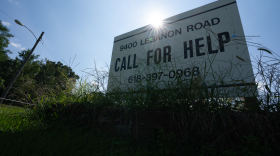 Standing on a sunny day behind tall grass next to to a road, Call for Help's sign advertises its location and phone number.  The nonprofit has provided resources for mental health, homelessness and other situations to Metro East residents.