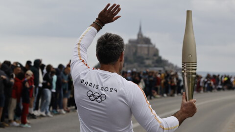 Torchbearer Maxime Gohier waves to the audience as he holds the Olympic torch in front of the Mont-Saint-Michel, Friday, May 31, 2024 in Brittany. (AP Photo/Jeremias Gonzalez)