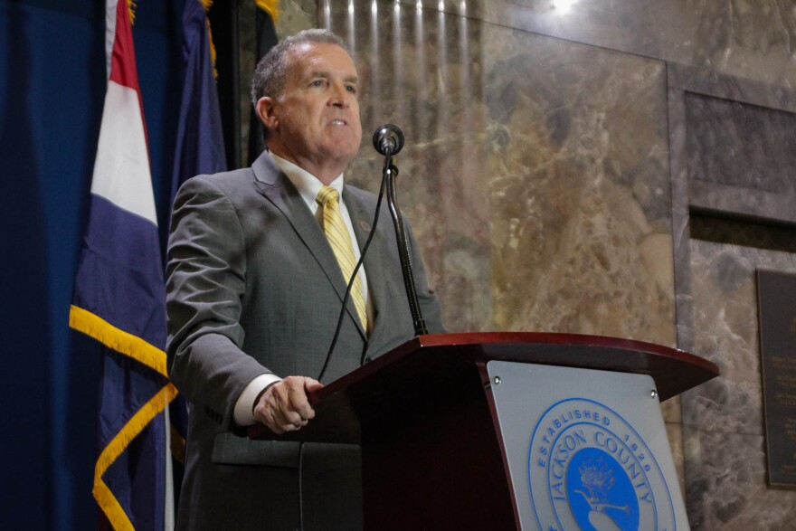 A man in a grey suit with a gold tie stands behind a podium. 