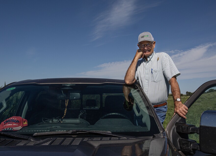 A man in a white shirt and hat with blue jeans stands behind a counter with buckets of potatoes