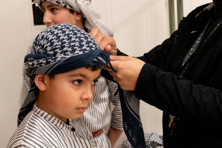 Adam Mutan stands as dance troupe coach Hanan Hamed fixes his keffiyeh on Saturday, Jan. 3, 2026 at First St. Charles United Methodist Church. 