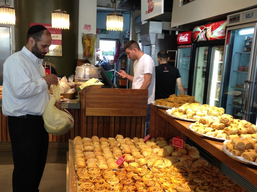 A man loads up on pastries at a Jerusalem shop. The shop owner says the new kosher rules are well-intentioned but will never fly.