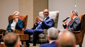 A woman and two men sit in large chairs 