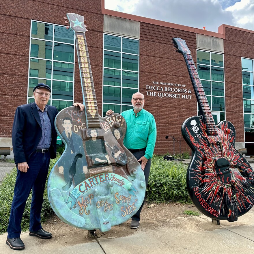 Fred Sauceman and Don Cusic pose near a giant guitar decorated with the Carter Family, in front of The Historic Site of Decca Records & the Quonset Hut
