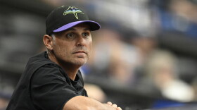 Tampa Bay Rays manager Kevin Cash wearing a baseball cap and leaning against a rail, looking into the distance