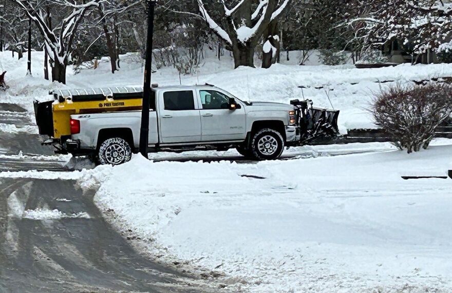 A pickup truck with a snowplow on the front and salt-spreader on the back plowing a residential driveway