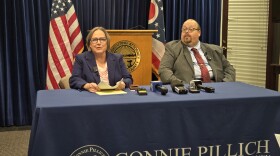 A man and a woman sit at a table in front of microphones