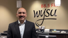 Juan Santiago facing the camera smiling with the words "88.5 FM WYSU" behind him on the wall