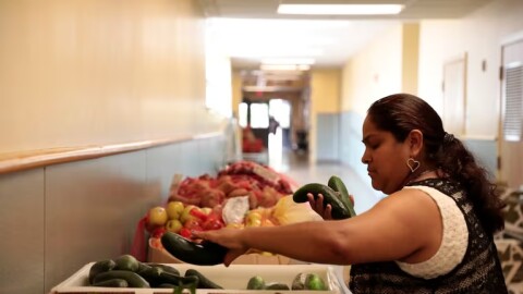 In this undated photo provided by the Oregon Food Bank, volunteer and food bank recipient Maria A. Rojas-Mendoza picks up vegetables at the Free Food Market run by Oregon Food Bank at Earl Boyles Elementary School. Last year, 2.5 million people visited free food sites in Oregon and southwest Washington last year, a 31% increase from the year before.