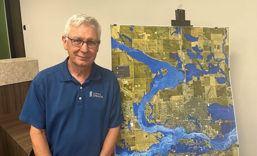 A man in a blue collared, short sleeve shirt stands next to a map of a river.