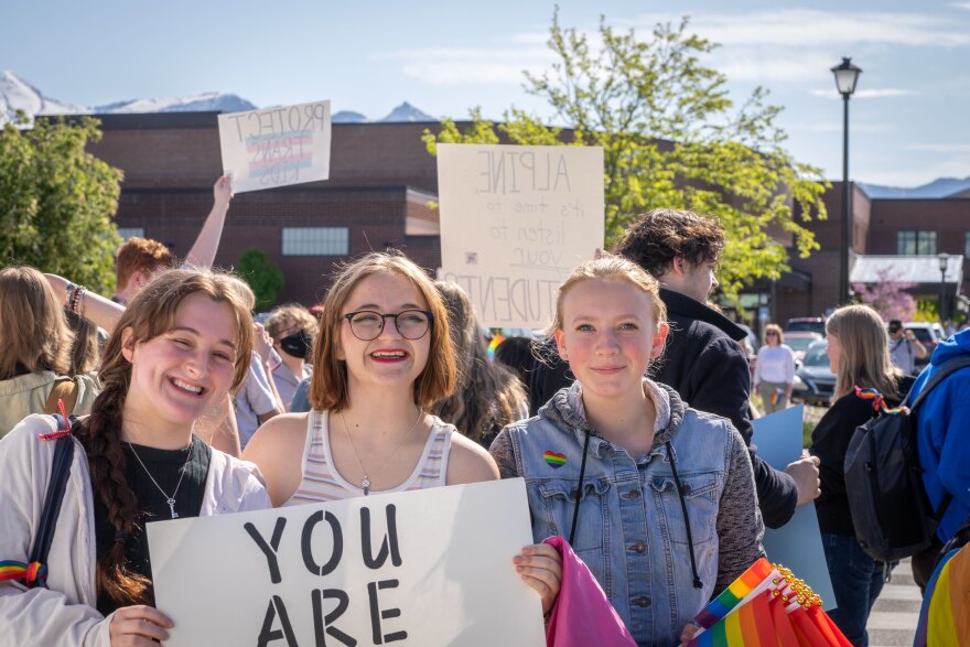 Skyridge High School senior Cameron Carnes, junior Olivia Brown and sophomore Erin Holmstead stand on the sidewalk across the street from their school after walking out of class in protest on May 15, 2023. All three students worked to protest the removal of pride flags from their school. They hold a sign that reads “You are loved.”