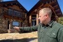 A man motions toward a log cabin.