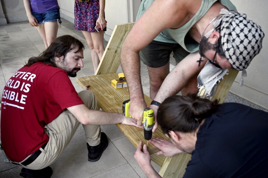 Andrew Rice driving in screws as members of the CT-DSA and volunteers assemble a wooden bench in front of an Eastern Orthodox Church by Bridgeport Hospital on 7/12/25. The bench is the first of its kind built by the CT DSA in Bridgeport, taking inspiration from similar actions in Hartford.