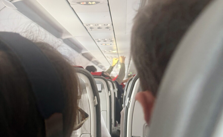A passenger holds an IV saline bag above the aisle as medical volunteers respond to an in-flight emergency aboard a flight approaching Ben Gurion Airport near Tel Aviv, Israel, on October 17, 2026. The aircraft encountered turbulence as passengers and crew worked to stabilize a woman experiencing difficulty breathing.