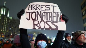A protester holds a sign reading "ARREST JONATHAN ROSS" during a rally for Renee Good, Thursday, Jan. 8, 2026, in Minneapolis, after she was fatally shot the day before.