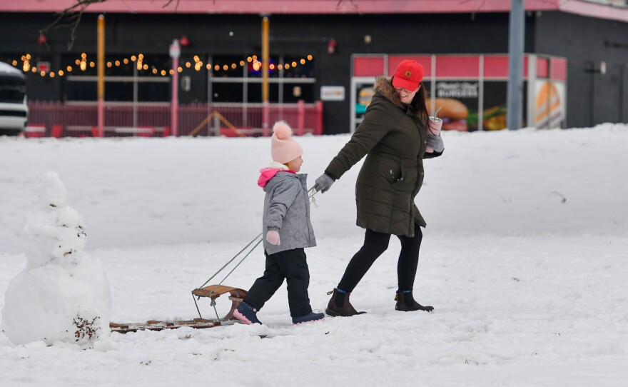 A pair of people pass a snowman on their way to go sledding.