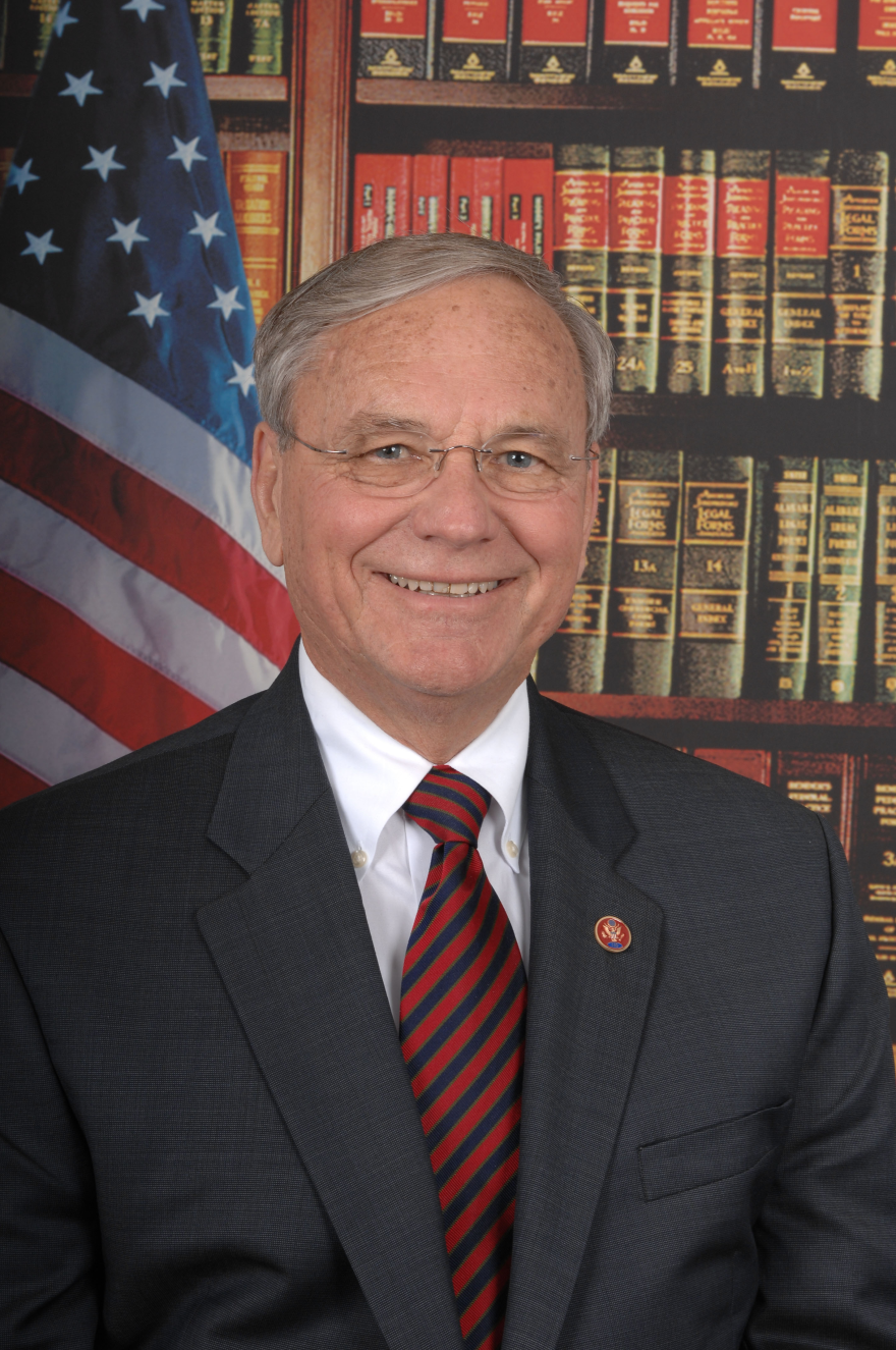 Older man in black suit with red tie wearing glasses