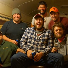 Six young men drinking beer in an old schoolbus, laughing