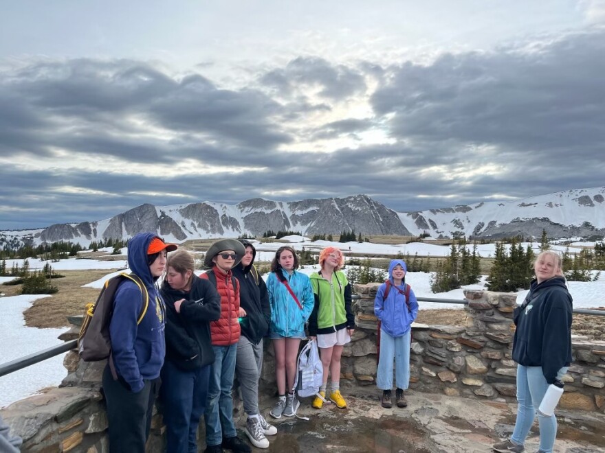 A group of seven kids and an adult pose in front of a mountain