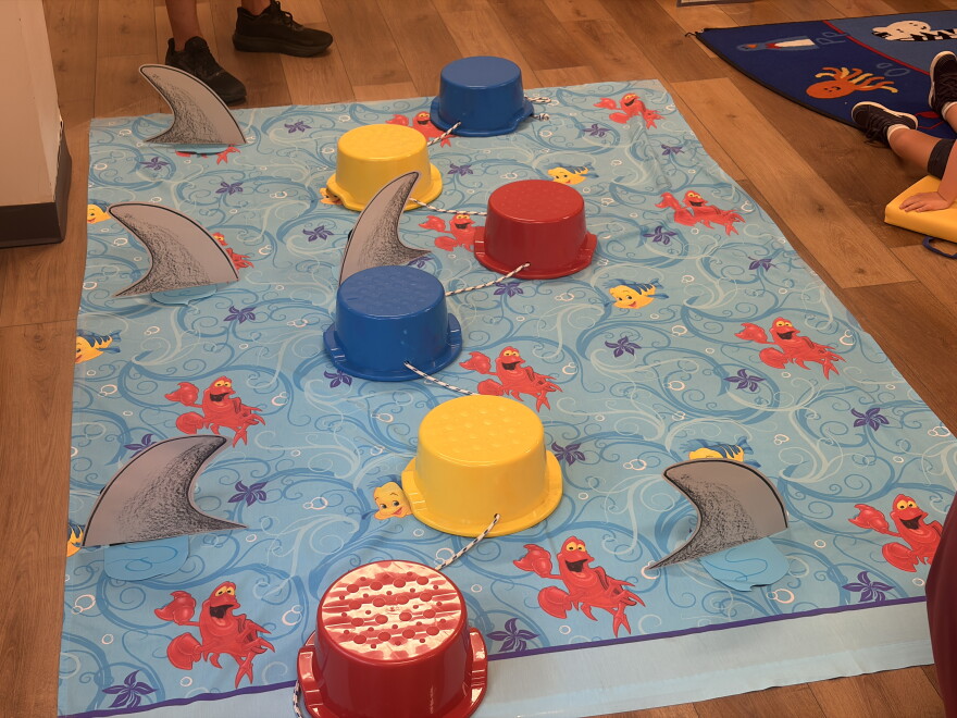 A blue mat with cutout shark fins and blue, yellow and red bowls on top.