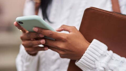 This stock image shows a female student holding a smartphone in her hands.