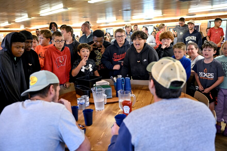 The boys cheer their perspective College League Deans during a french fry eating challenge between their 2 teams as the lunch break ends at Experience Camps, a free grief camp for kids whose parent died, expanded to Connecticut this year at Camp KenWood and KenMont, in Kent, Connecticut August 20th 2025.