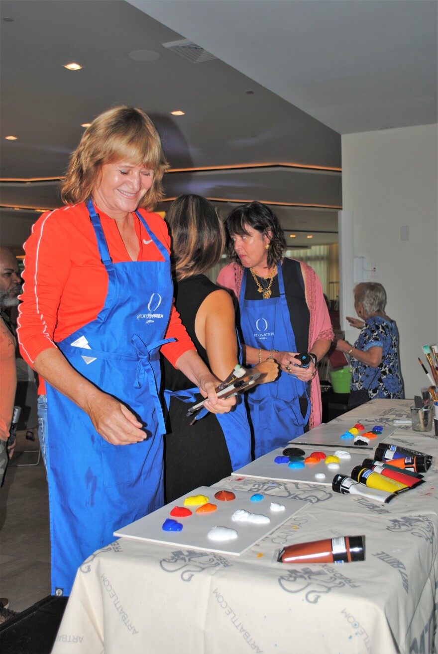Artists stand before a table of paint