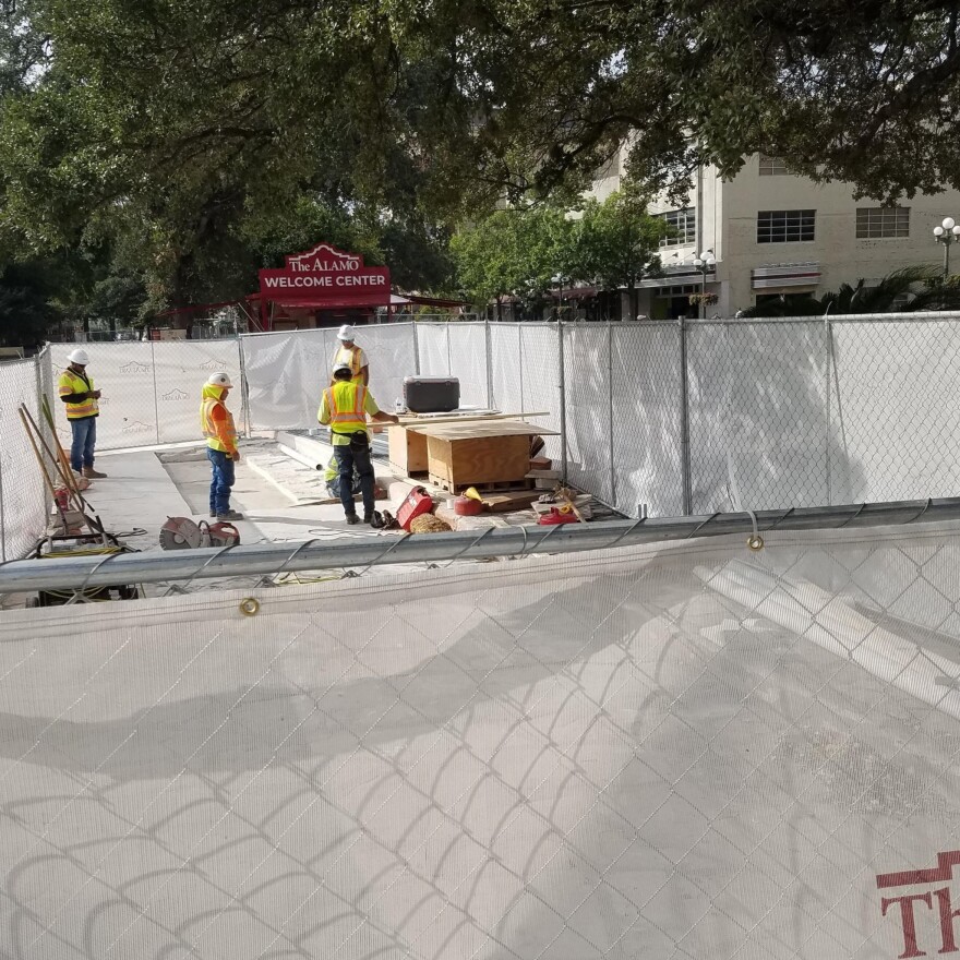 A peek over the fence shows construction workers on Alamo grounds.