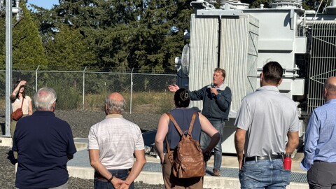 Jeff Nelson is standing in front of an electrical installation. He is holding a mic and gesturing.