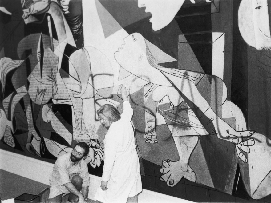 Museum of Modern Art employees clean spray paint off of Pablo Picasso's mural <em>Guernica</em> shortly after Tony Shafrazi wrote "Kill lies all" on it in 1974.