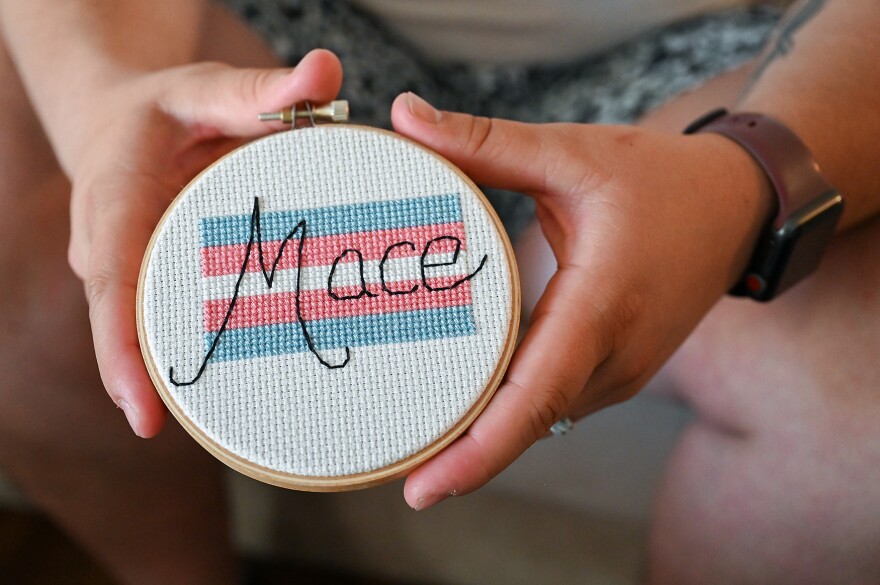 Mace Hoover holds a cross stitch of a trans pride flag bearing his name on Wednesday, May 22, 2024, at his apartment in Columbia. “My friend Tim, another queer music teacher in Columbia, made it for me. He was one of the first people I told when I came out and felt safe enough to tell because he himself was queer, but I had also watched him encourage and support his students in their identities as well,” Hoover said. “Music has gotten me through every step in this journey. Since I was a child, I think I was, for lack of a better word, singing before I could speak in a lot of ways. … So music’s always been a really big part of who I am and who I was meant to be, I believe.”