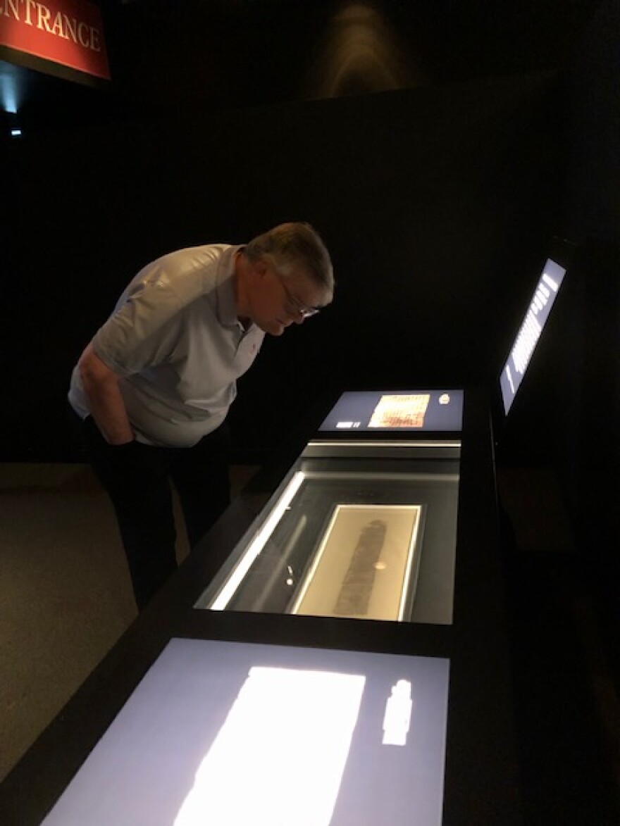 A man leans over to inspect a case holding a parchment.