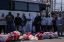 A number or men line up next to a bus while a man with a 'Police ICE' vest speaks to some of them. 