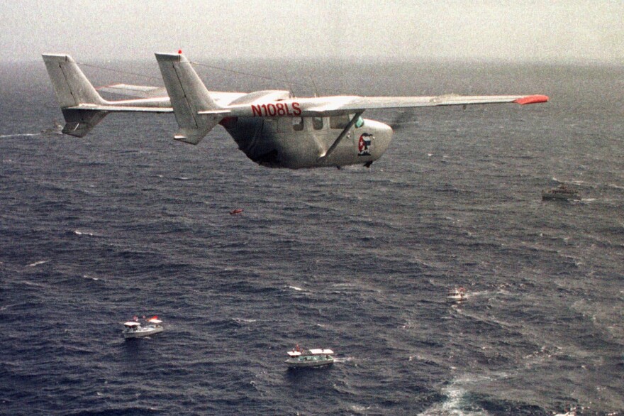 A plane is seen flying above three boats at sea