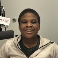 A head and shoulders image of Bloomington Junior High School student Erioluwa Jegede sated at a WGLT microphone. He wears a white running jacket