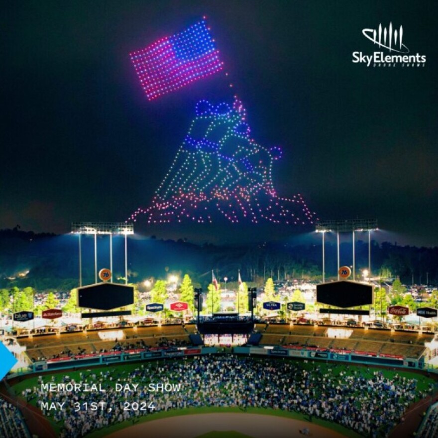 Drones on a night sky depict the Marine Corps War Memorial, with soldiers gathered around an American flag