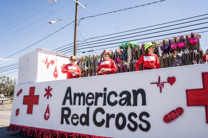 Three people stand on a float with "American Red Cross" and the iconic Red Cross painted along the side. 