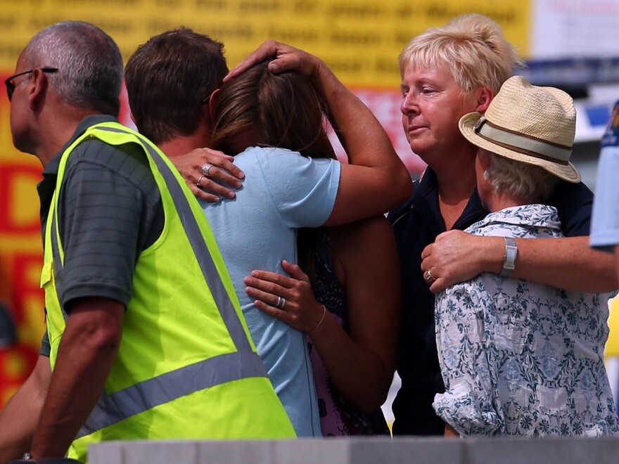 People grieve outside New Zealand's Muriwai Surf Lifesaving Club after the fatal shark attack at Muriwai Beach on Wednesday.