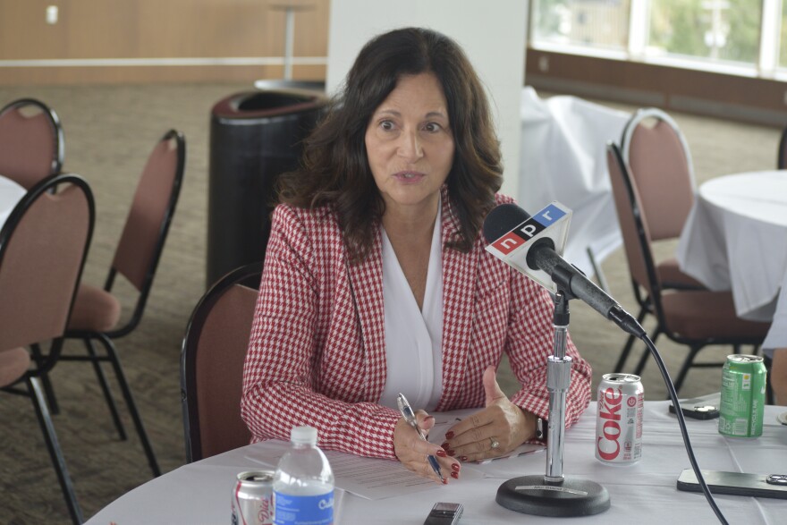 ISU Athletics Director Jeri Beggs seated at a roundtable in front of a microphone wearing a red checkered jacket and white top.