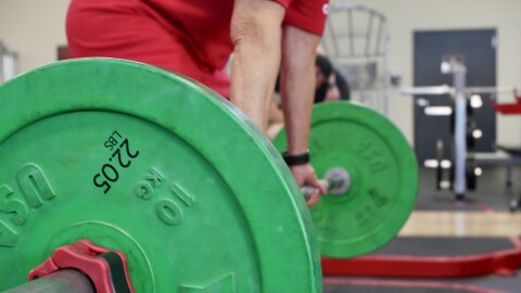 An older woman lifts a bar with large green weights on each end.