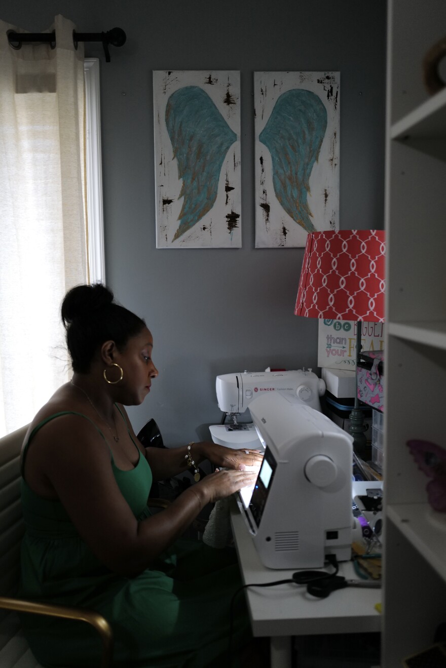 Heather Wilson sews an angel gown beneath a pair of angel wing paintings in her Virginia Beach home.