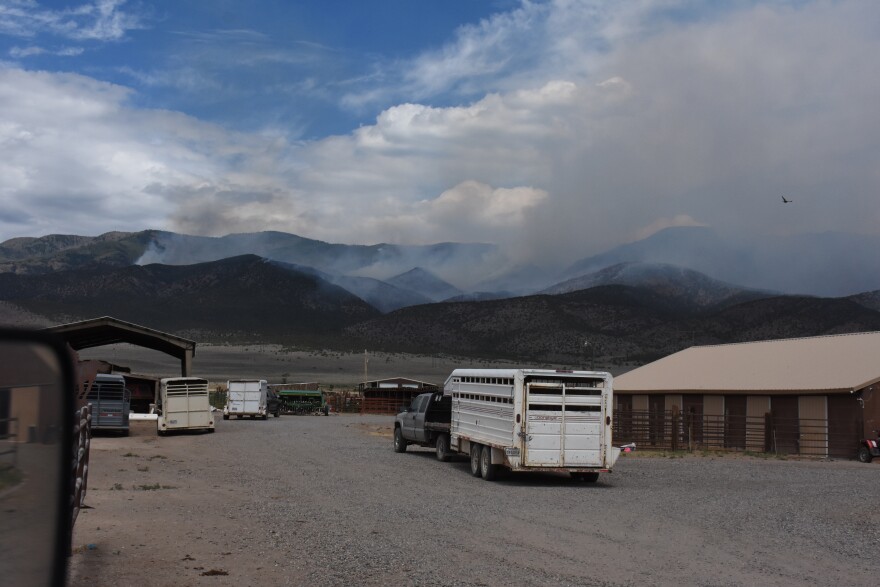 In an undated photo provided by Emma Wilde, smoke rises from the Cottonwood Fire near a field with trucks and cattle trailers ready to evacuate.