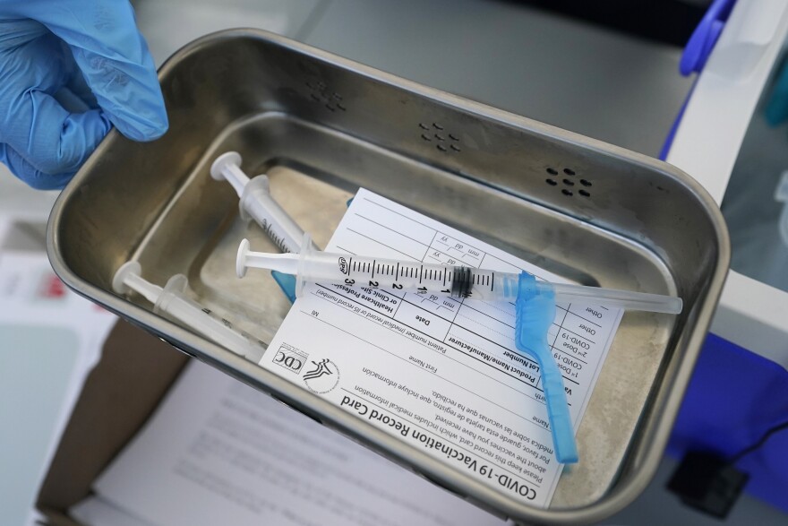 Syringes sit in a bin on top of a COVID-19 vaccination card