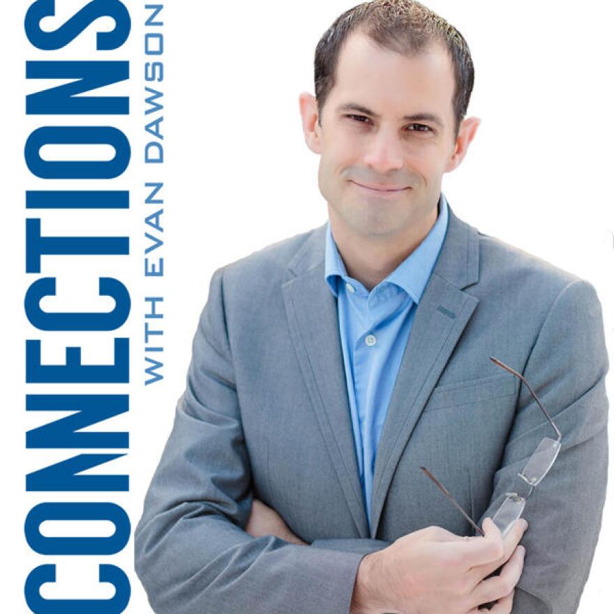 A smiling man with short dark hair wearing a blue button-down shirt and a grey blazer. He is holding a pair of eyeglasses. The word "Connections" appears on the left side of the photo in vertical letters.