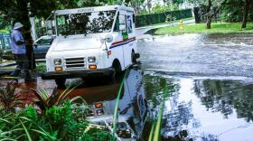 In this June 19, 2019 file photo, a postal worker returns to their truck parked on a flooded street in Miami caused by high tides.