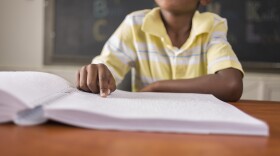 A stock photo of a young African-American boy sitting in class reading a braille book.